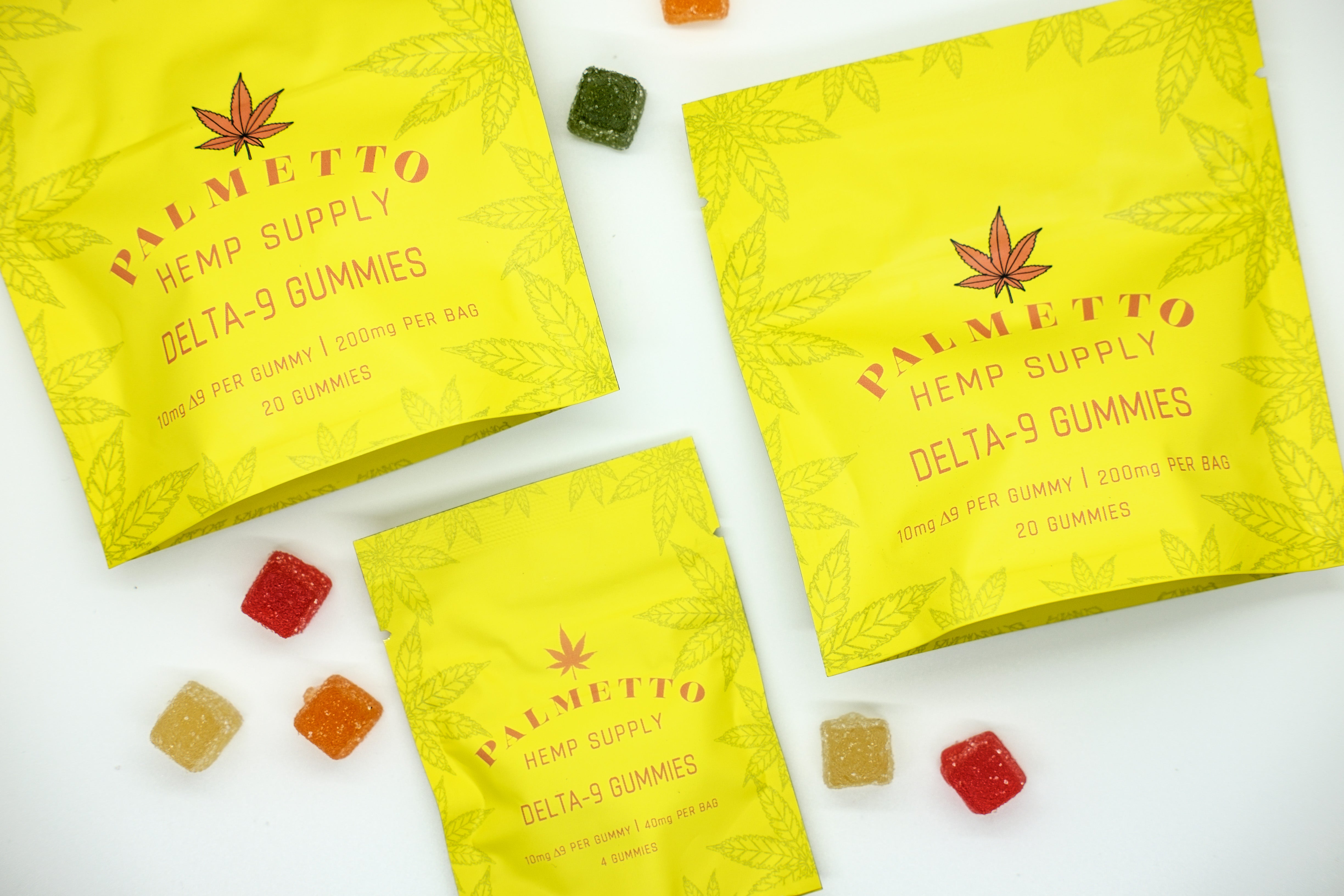 Yellow bags of Palmetto Hemp Supply delta-9 gummies on a white background with various colored gummies in between the bags.