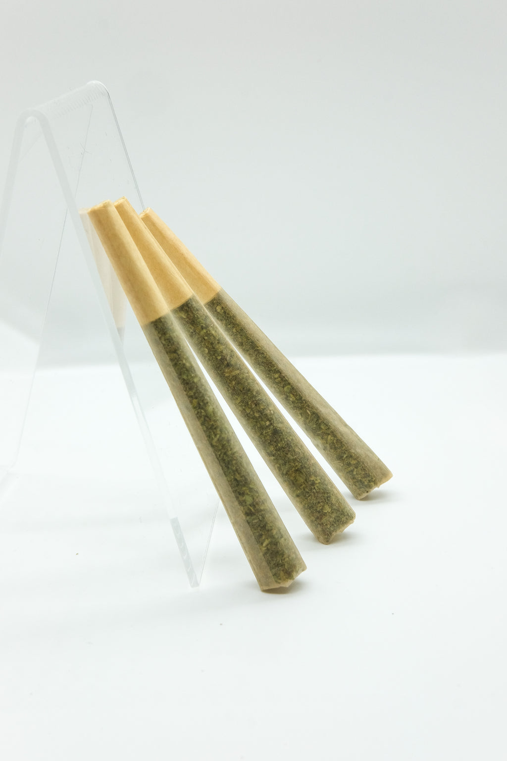 Three pre rolls leaning on a clear acrylic stand on a white background 