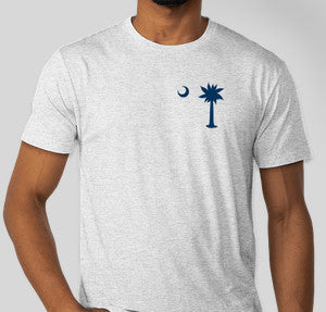 Person wearing a heathered white t-shirt with a navy palmetto tree and half moon logo on the top left side of the shirt front.